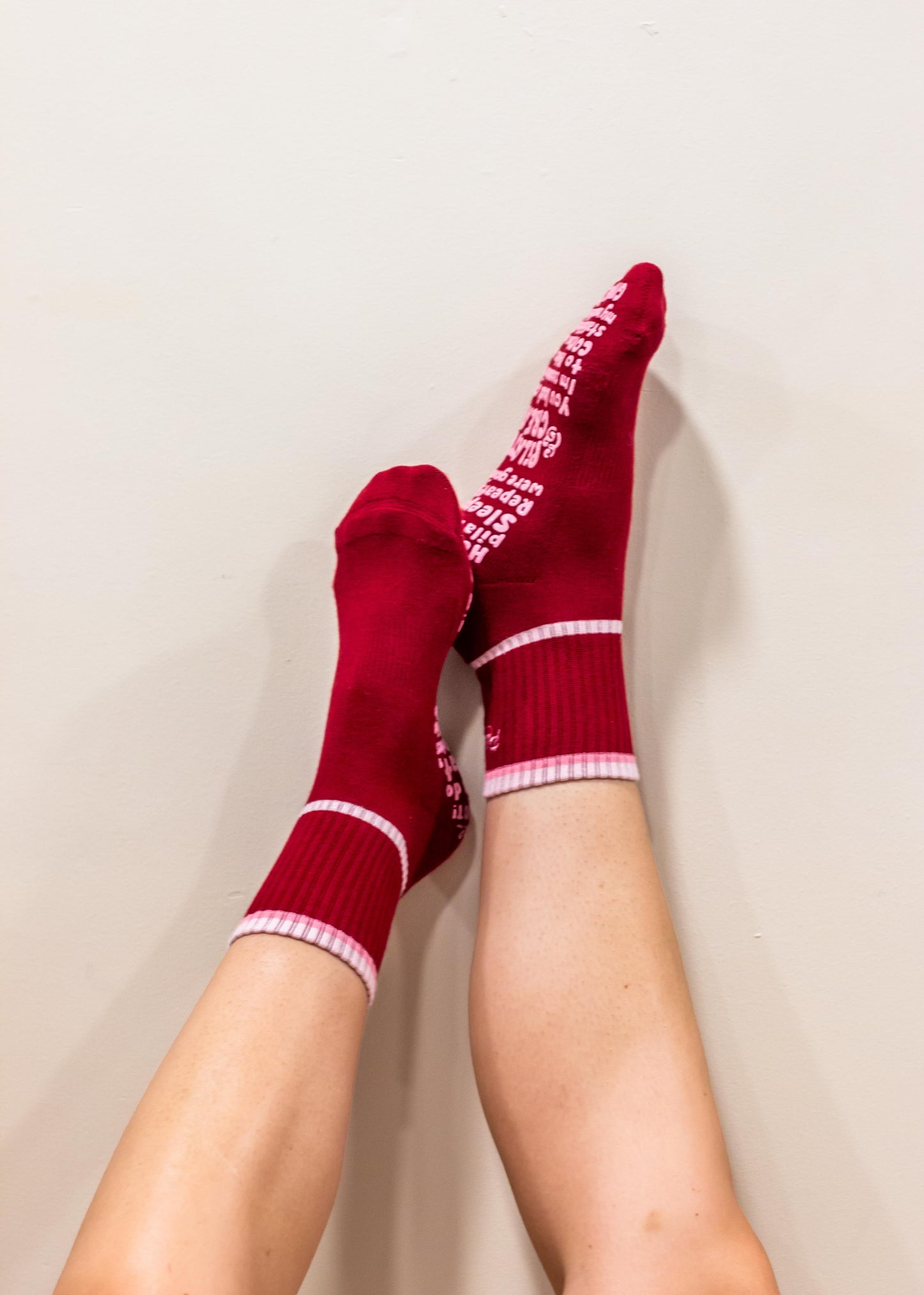 burgundy socks with pink tonal tipping around ankle with white text and stripes worn by a person on a plain background